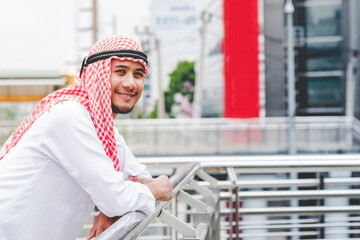 Portrait Islamic man smile look at camera wear muslim dress in modern uae city. Arab men wear hijab...