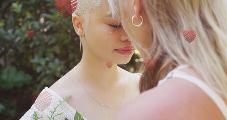Image of hearts falling over diverse female couple embracing