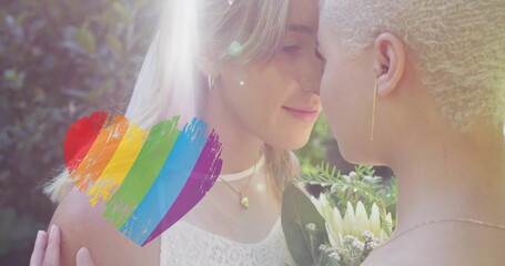Image of rainbow heart over diverse female couple embracing