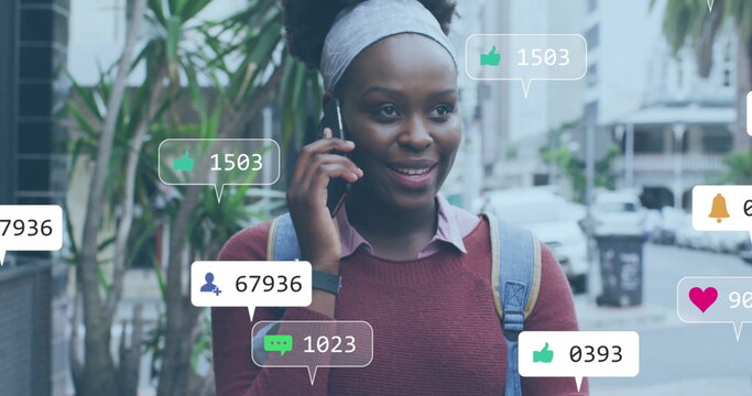 Image of media notifications over african american woman talking on smartphone in city