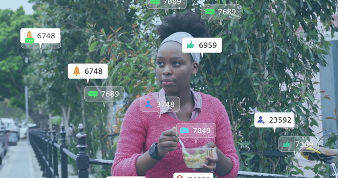 Image of media notifications over african american woman eating in city street