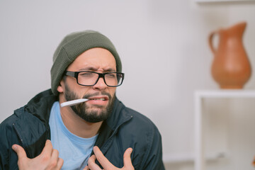 Sick young man measuring body temperature with thermometer