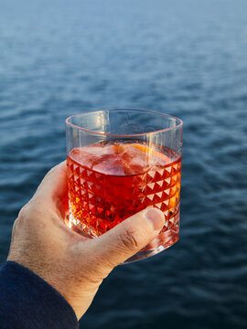 Hand holding a glass of Negroni cocktail over the ocean view.