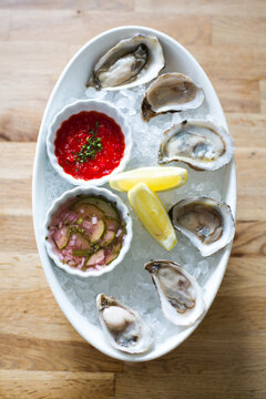 Birds eye view of a plate with fresh oysters on the shell with mignonette and cocktail sauce with a lemon wedge over plate filled with ice.