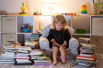 Little Caucasian blonde girl reading books in the evening. Little reader. Early Education concept....