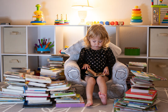 Little Caucasian blonde girl reading books in the evening. Little reader. Early Education concept. Baby and books