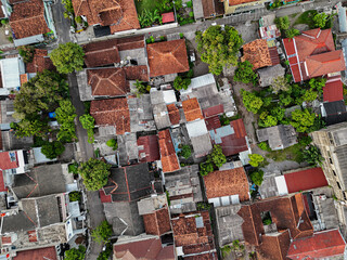 A vibrant aerial view of a tightly-knit urban neighborhood showcases a mosaic of rooftops and narrow streets. The density of residential houses in Yogyakarta, Indonesia.