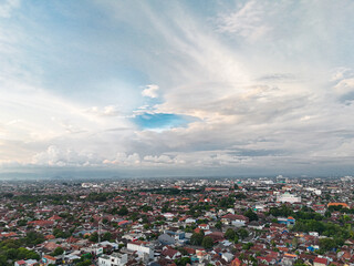 A peaceful aerial view of Yogyakarta city in the late afternoon, capturing the sprawling rooftops beneath a soft, cloud-filled sky as daylight begins to fade