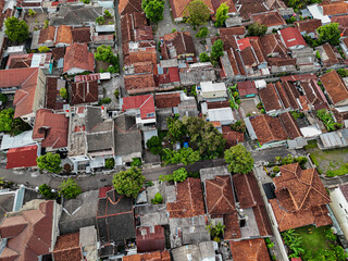 A vibrant aerial view of a tightly-knit urban neighborhood showcases a mosaic of rooftops and narrow streets. The density of residential houses in Yogyakarta, Indonesia.