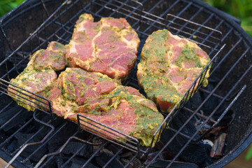 Herb-Crusted Pork Cuts Prepared for Grilling. Raw Steaks with Green Marinade on Charcoal Barbecue