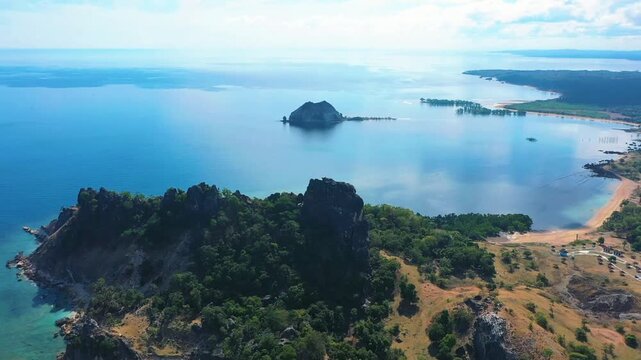 Aerial view of a small island surrounded by water with lush green vegetation, terrestrial plants, trees, and a beautiful natural landscape including a beach and reef