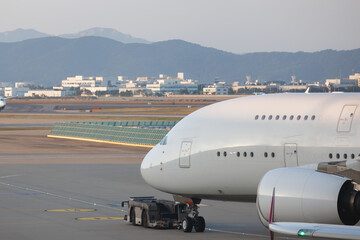 Fototapeta premium Large white jumbo jet airplane is parked in the airport, with airport tow truck in front of it during taxi to runway. Concept of air transportation and plane mockup.