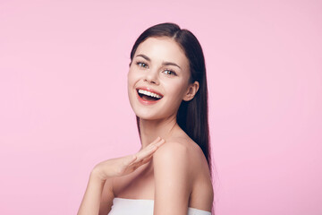 Beautiful young woman with a cheerful smile, hands on face, on a pink background