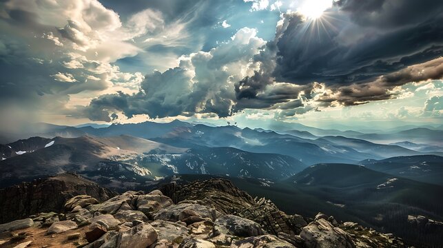 Rocky mountain range with dramatic clouds rolling over midday sun