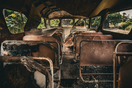 Interior of an abandone school bus with shatered windows and benches in the outside. 