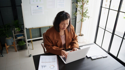 Mature business asian woman entrepreneur in office using laptop. 60s businesswoman with technology asian senior woman