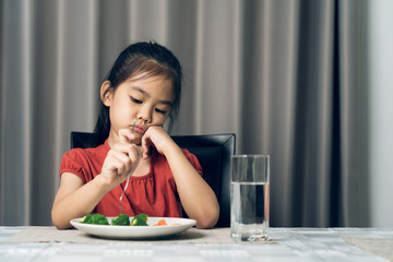 Little cute kid girl refusing to eat healthy vegetables. Children do not like to eat vegetables.