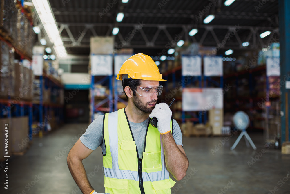 Wall mural Portrait of caucasian man worker working using walkie-talkie in huge spacious warehouse retail store industry factory. Cargo in ecommerce transport and logistics, Rack of stock storage with carton box