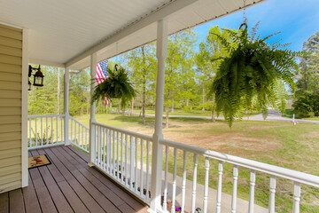 A Porch With Hanging Ferns And An American Flag In The Background On A Sunny Day