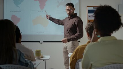 Medium shot of young Caucasian male school teacher explaining new material about continents to unrecognizable teenage students sitting at desks in classroom and listening - Powered by Adobe
