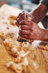 Carpenter using hand plane on wood with shavings in workshop