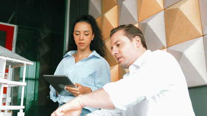 Portrait of project manager pointing at house model while discussion about building design. Caucasian cooperative architect engineer team brainstorming about building material. Teamwork. Manipulator.