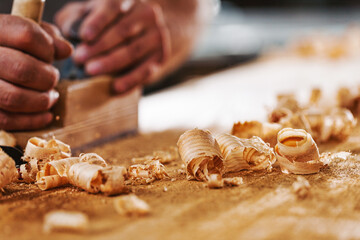 Carpenter using hand plane on wood with shavings in workshop