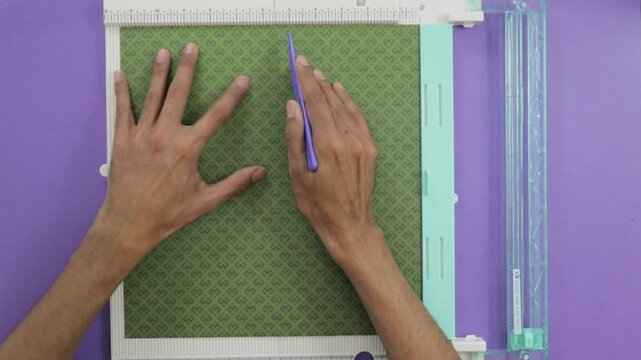 Woman is making fold marks on patte rned green paper with the score board tool, negative and copy space for text
