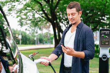 Man using smartphone online banking application to pay for electric car battery charging from EV...
