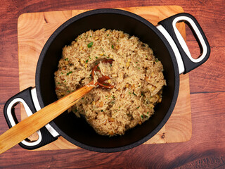 Iç pilav - Turkish rice with currants and pine nuts in a black pot, set on a wooden board, stirred with a wooden spoon