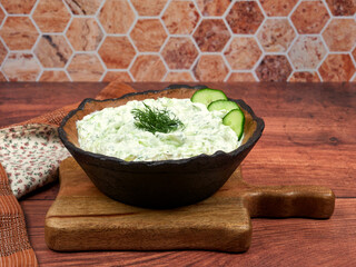 A bowl of Tzatziki, a creamy Greek yogurt dip with finely chopped cucumbers, garlic, and dill, set...