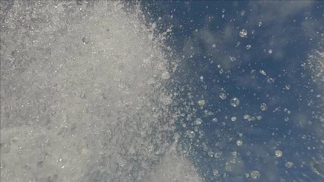 Gush and splash of water of fountain falling from above on the camera on blue sky background, bottom view, slow motion, close-up.
