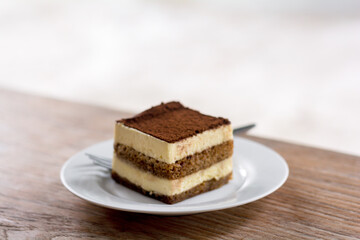 Close up a piece of tiramisu with mascarpone cream and biscuits on a white dish and wooden table.....