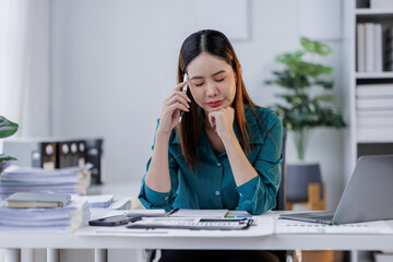 Asian woman in the workplace Work Hard writing notes on a pad from her laptop computer with analytical charts and graphs in front of her, business people concept