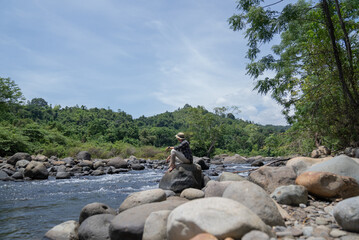 A man sits among the rocks on the banks of a tropical rainforest river