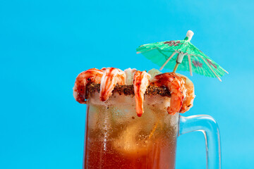 Michelada decorated with shrimp on blue background. Copy space.