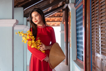 Vietnamese girl with Ao Dai dress standing in traditional house of Vietnam. Text in photo mean best wishes to family, happiness, prosperity, health. Tet holiday and New Year.