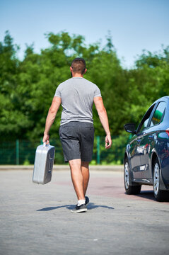 Young man walking along road to nearest gas station to fill canister. Male adult needs to refuel stalled car. Back view of man walking near road with canister in hand.
