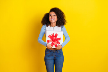 Photo of attractive young woman hold gift look up excited empty space dressed stylish blue clothes isolated on yellow color background