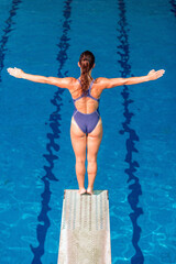 Female diver in white swimsuit, poised on the diving board, ready for a high dive. Captures the...