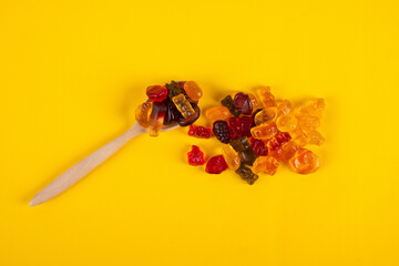 Colorful candies, jelly and marmalade with spoon on yellow background. 