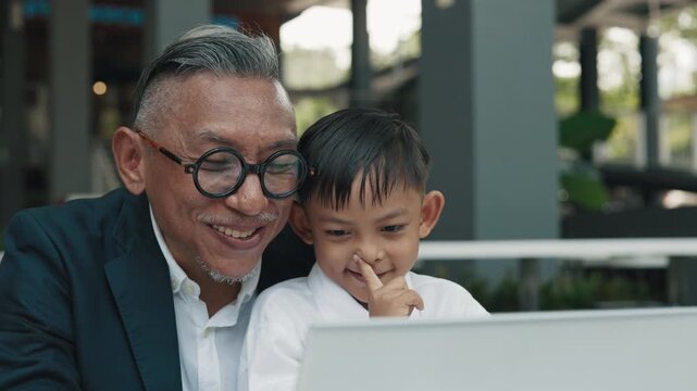 Asian family of father and little son wave hands to laptop camera in cafe slow motion. Happy single father shows schoolboy to relatives via computer. Parenting lifestyle