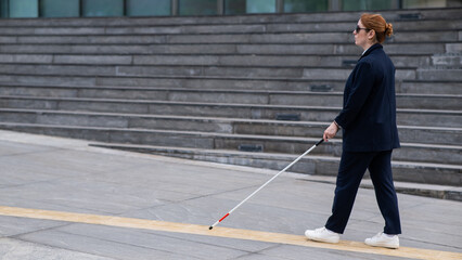 Blind businesswoman walking along tactile tiles with a cane. 