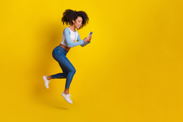 Full body photo of attractive young woman hold device running dressed stylish blue clothes isolated on yellow color background