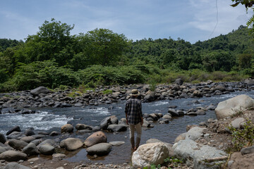 A man walks among the rocks on the banks of a tropical rainforest river