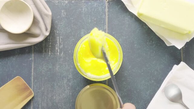 Pouring ghee butter into a pot with a knife. Cenital of knife pours creamy gui into a bowl. Slow motion