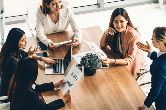 Businesswoman in group meeting discussion with other businesswomen colleagues in modern workplace office with laptop computer and documents on table. People corporate business work team concept. uds