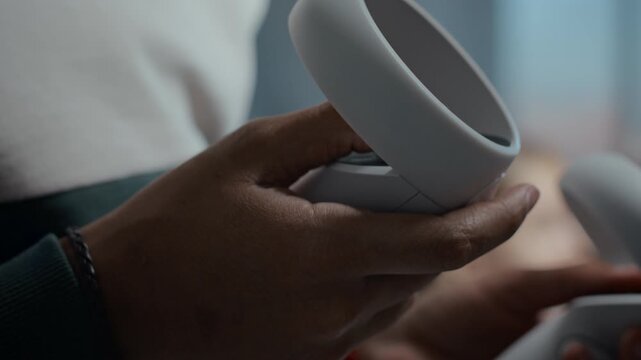 Extreme close-up of hands of child holding motion-sensing controllers providing tactile response while playing virtual reality game using VR headset