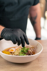 close up in a fast food establishment large chef in a black uniform prepares Japanese udon soup...