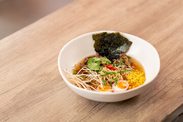close up in a restaurant on light table a white plate with Japanese udon soup with egg and noodles...